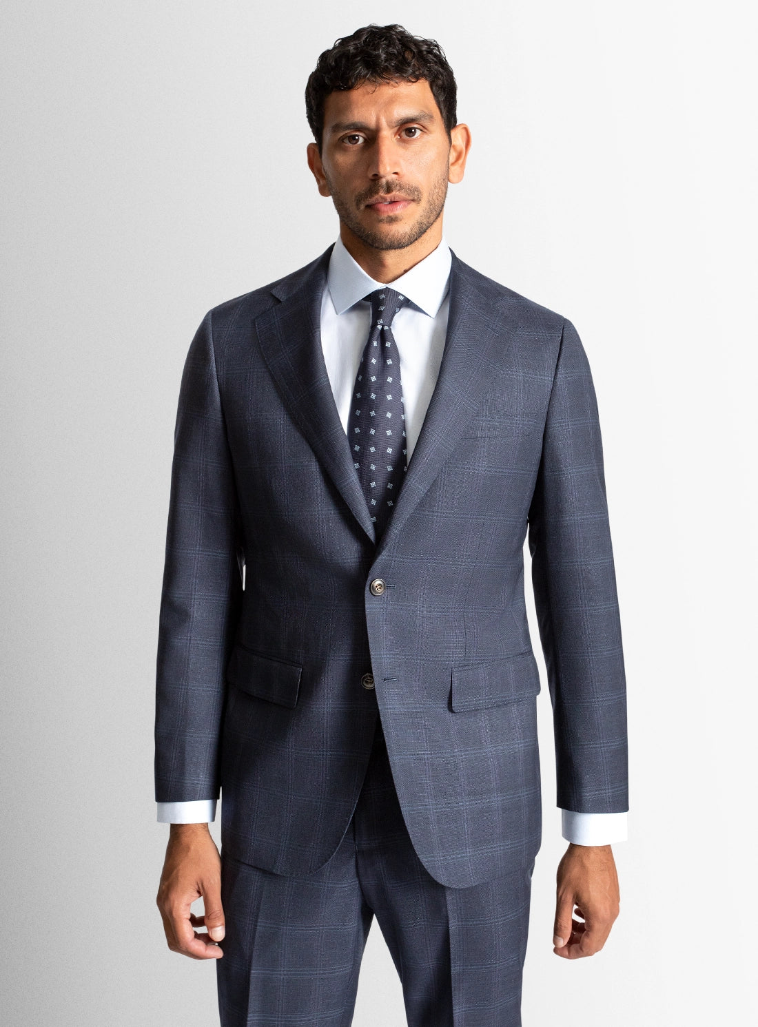 Man wearing a gray suit with a white shirt and patterned tie on a light gray background