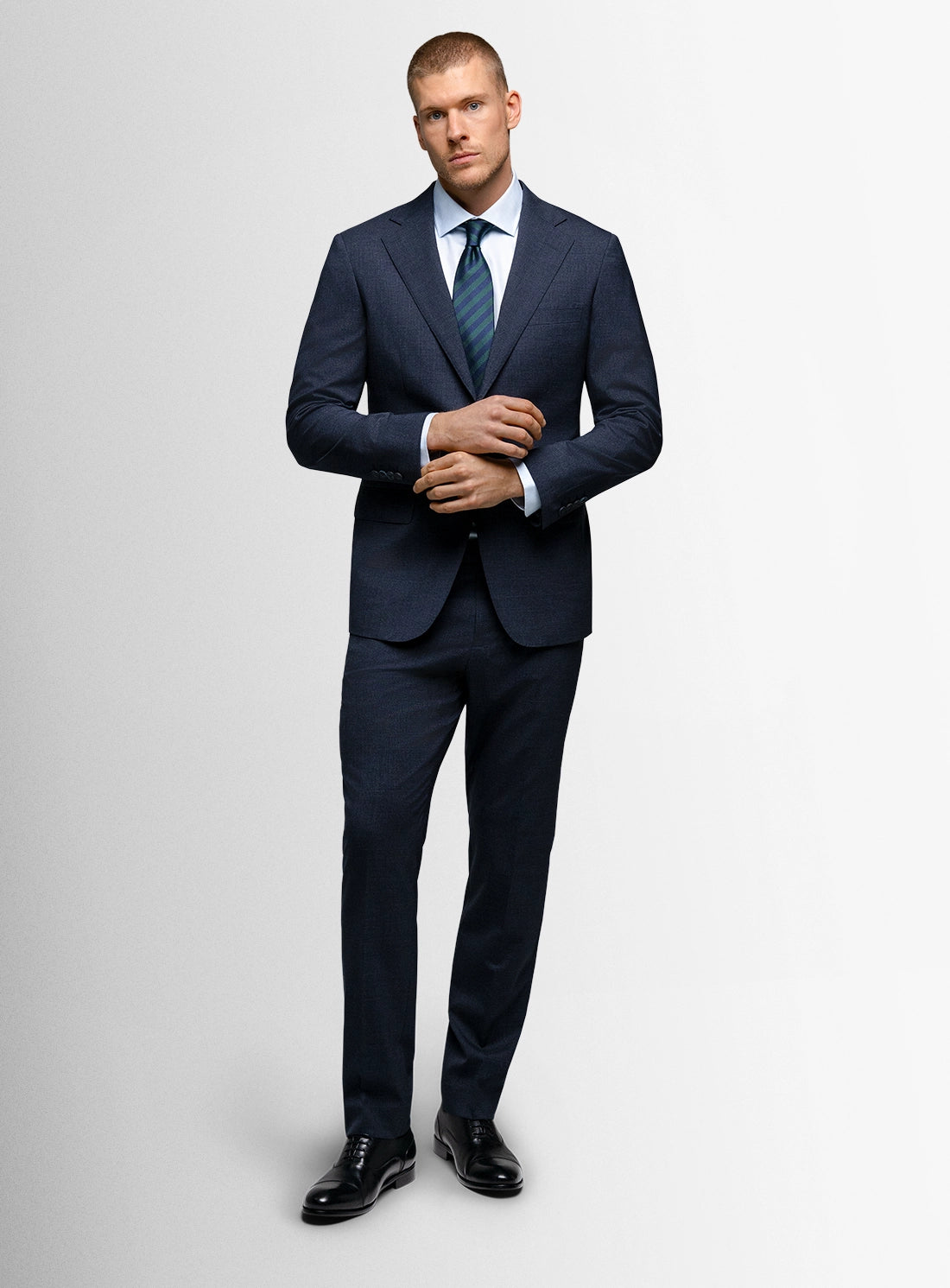 Man wearing a navy suit with a white shirt and black shoes on a light gray background