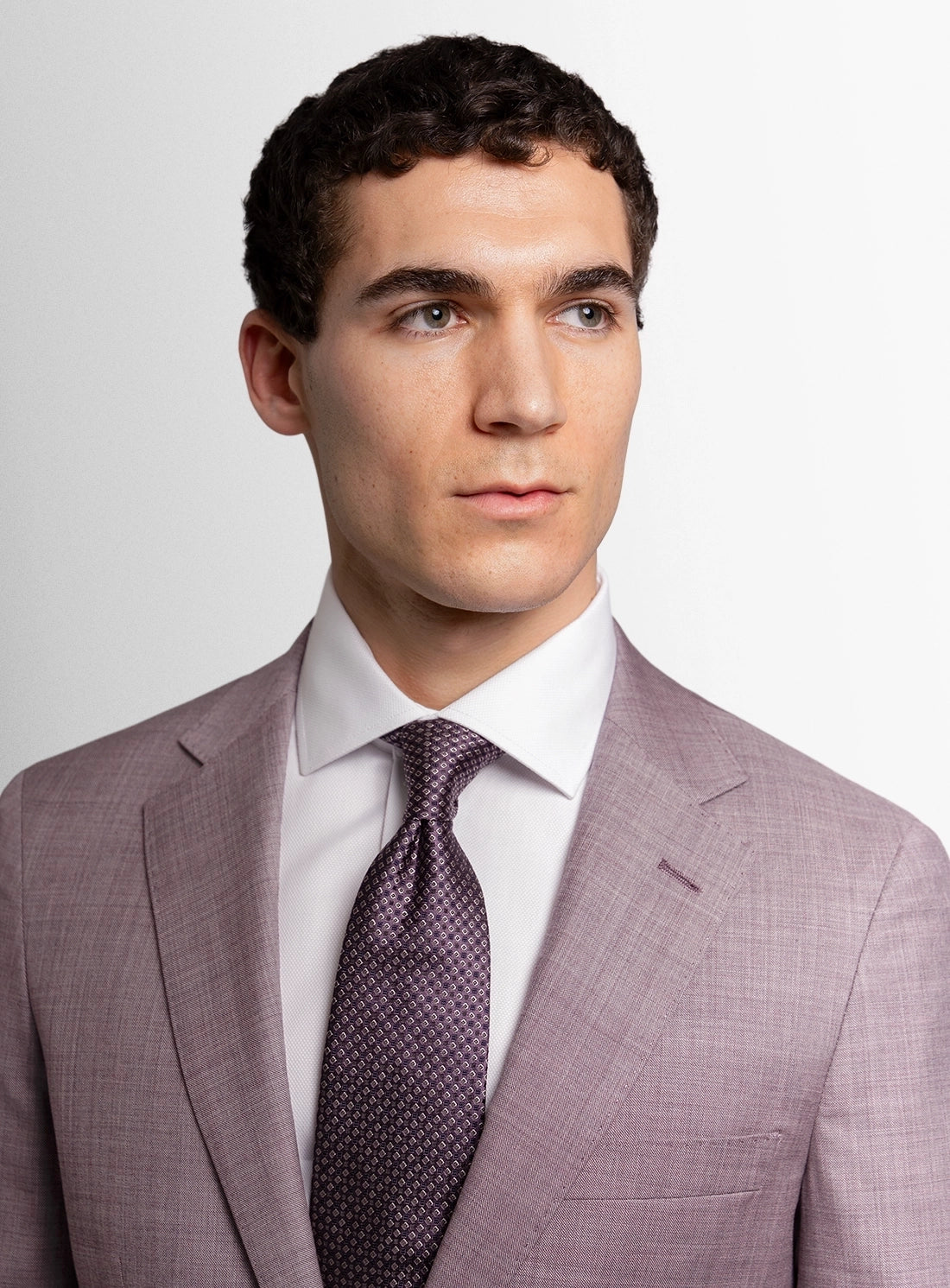 Man wearing a gray suit with a white shirt and patterned tie on a light gray background