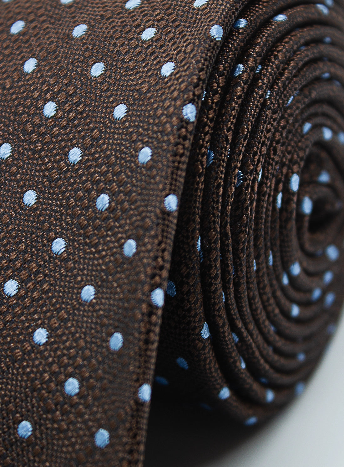 Close-up of a brown tie with blue polka dots, rolled up.