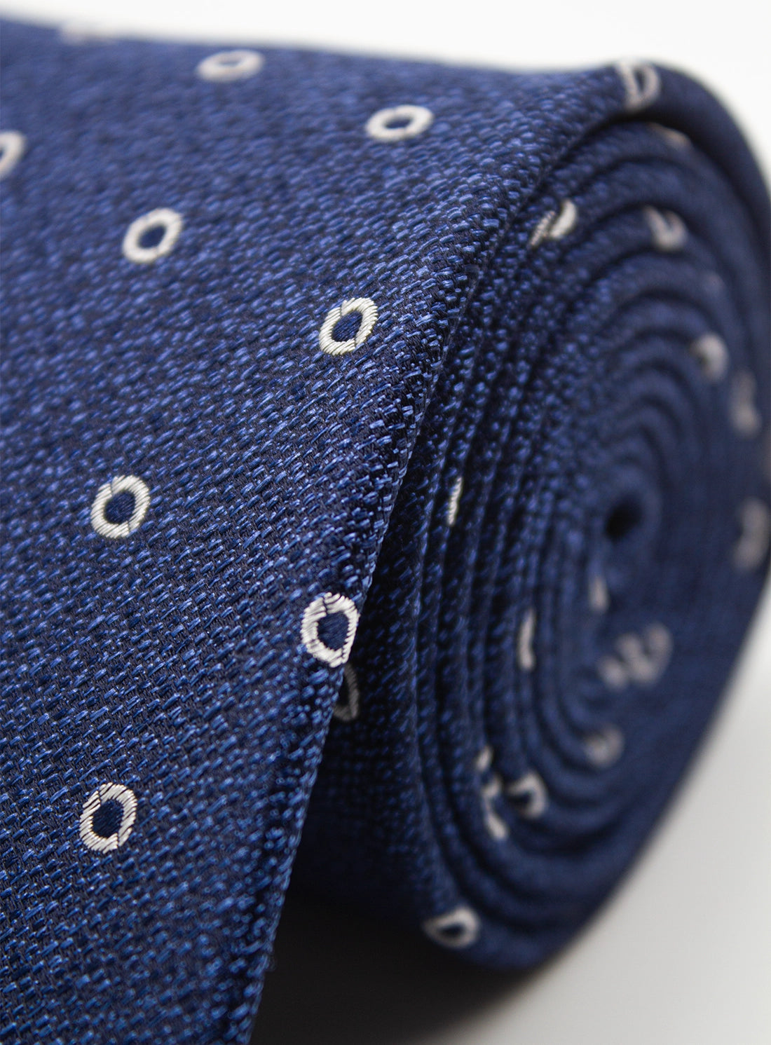 Close-up of a blue tie with white circular patterns on a light gray background