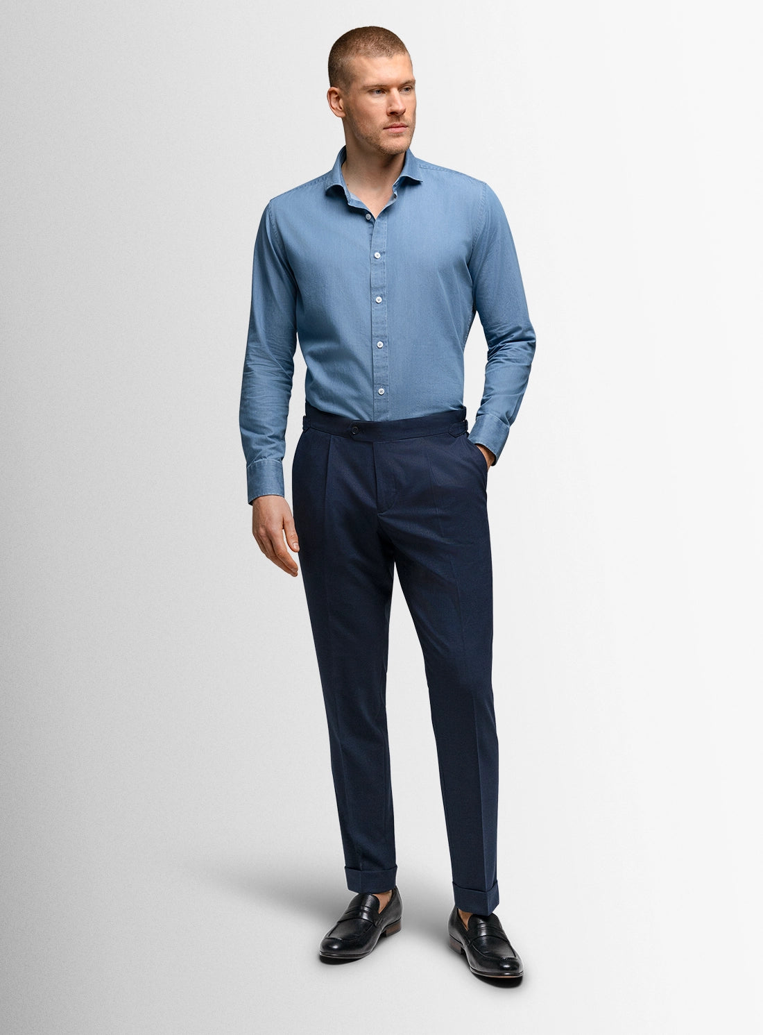 Man wearing a blue shirt and dark pants on a light gray background