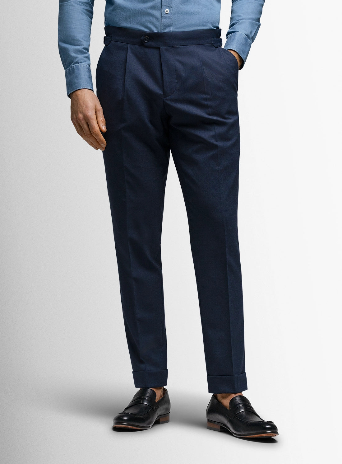Navy blue dress pants worn with a light blue shirt and black shoes on a white background