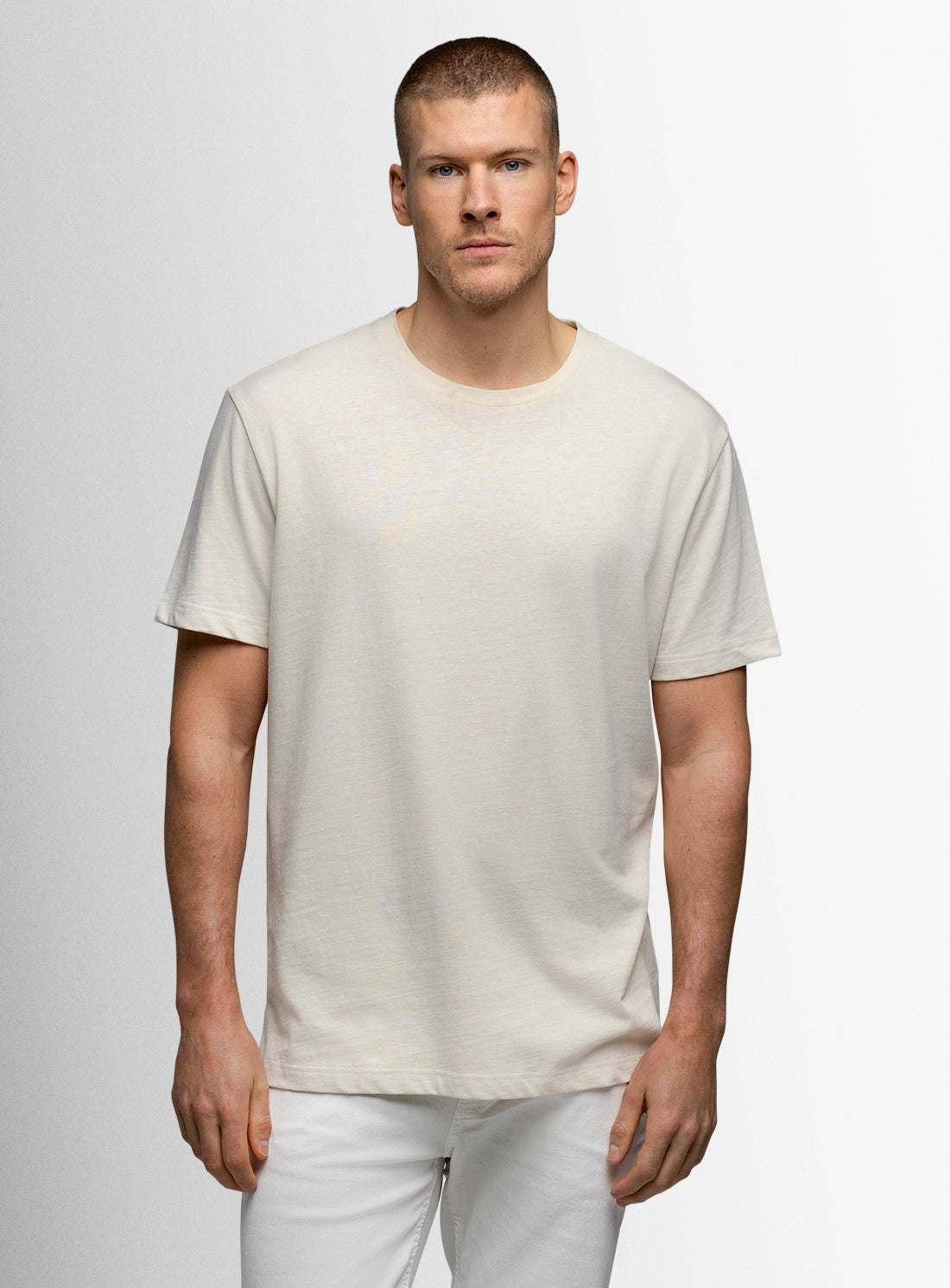 Man wearing a plain white t-shirt and pants against a light gray background