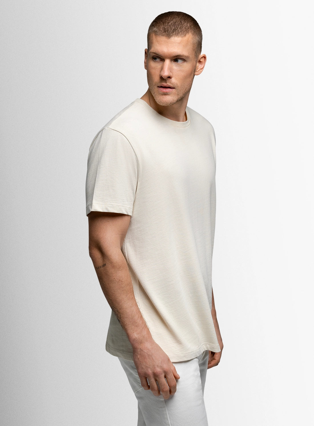 Man wearing a plain white t-shirt and pants against a light gray background