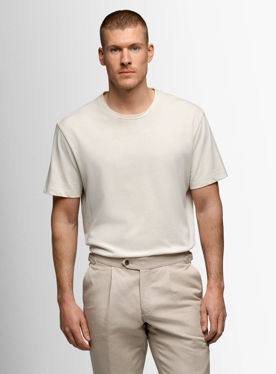 Man wearing a plain white t-shirt and beige pants against a light gray background