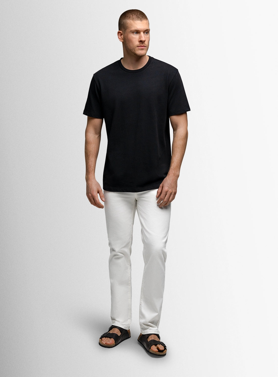Man wearing a black t-shirt and white pants on a plain background