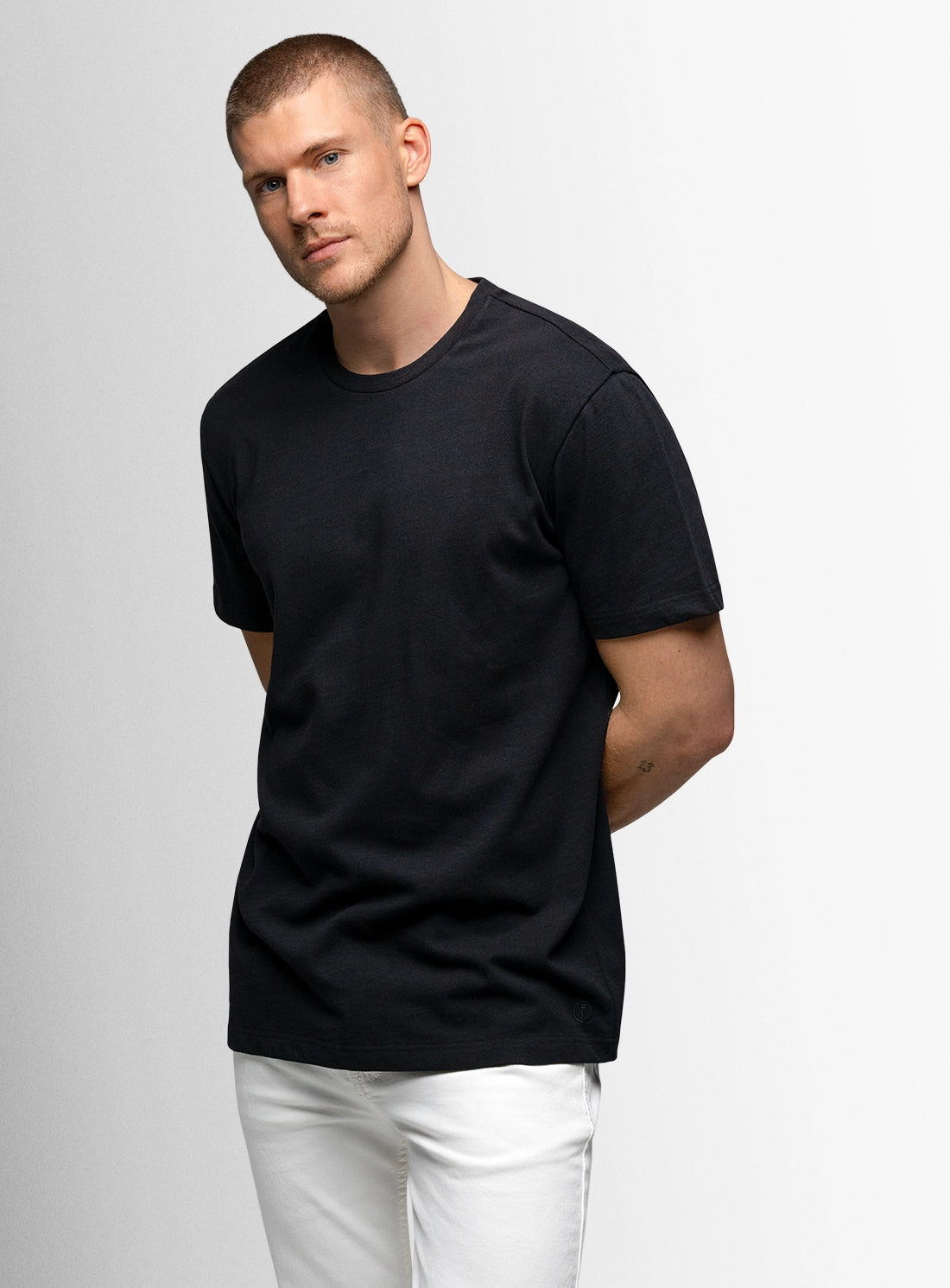 Man wearing a black t-shirt and white pants on a light gray background