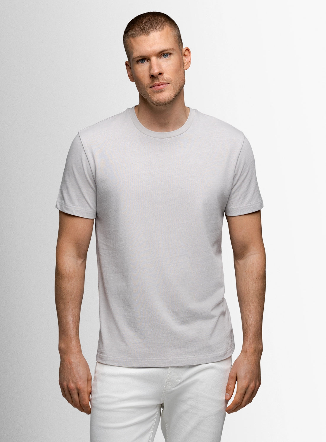 Man wearing a plain gray t-shirt and white pants against a light gray background
