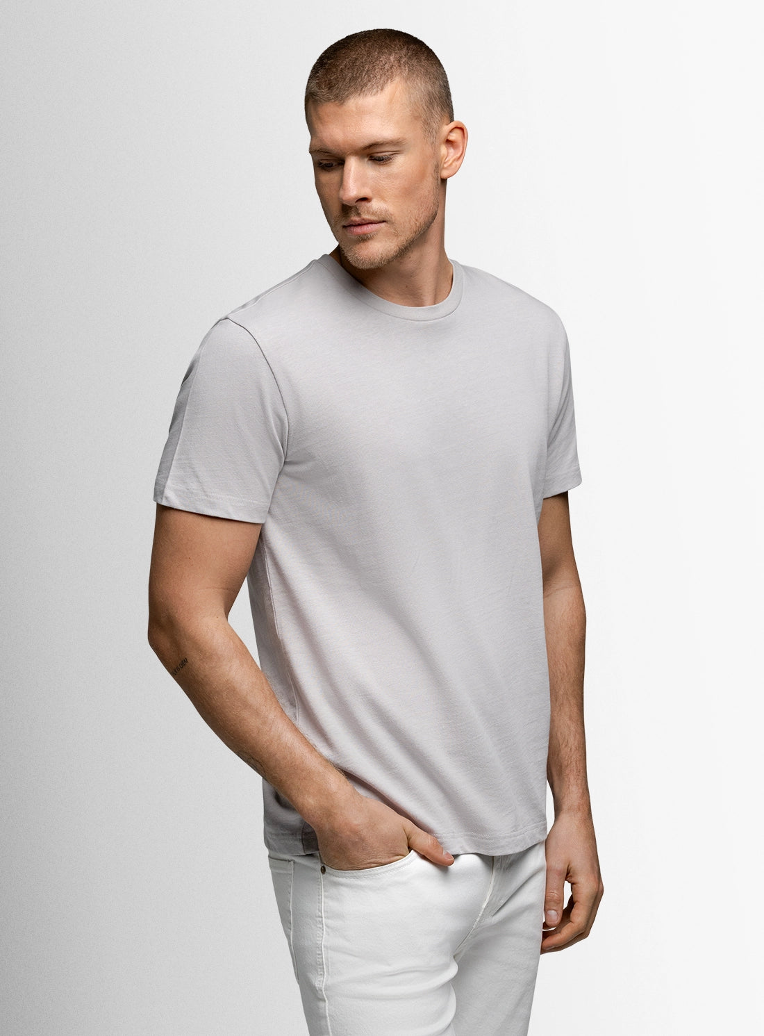 Man wearing a light gray t-shirt and white pants against a plain background