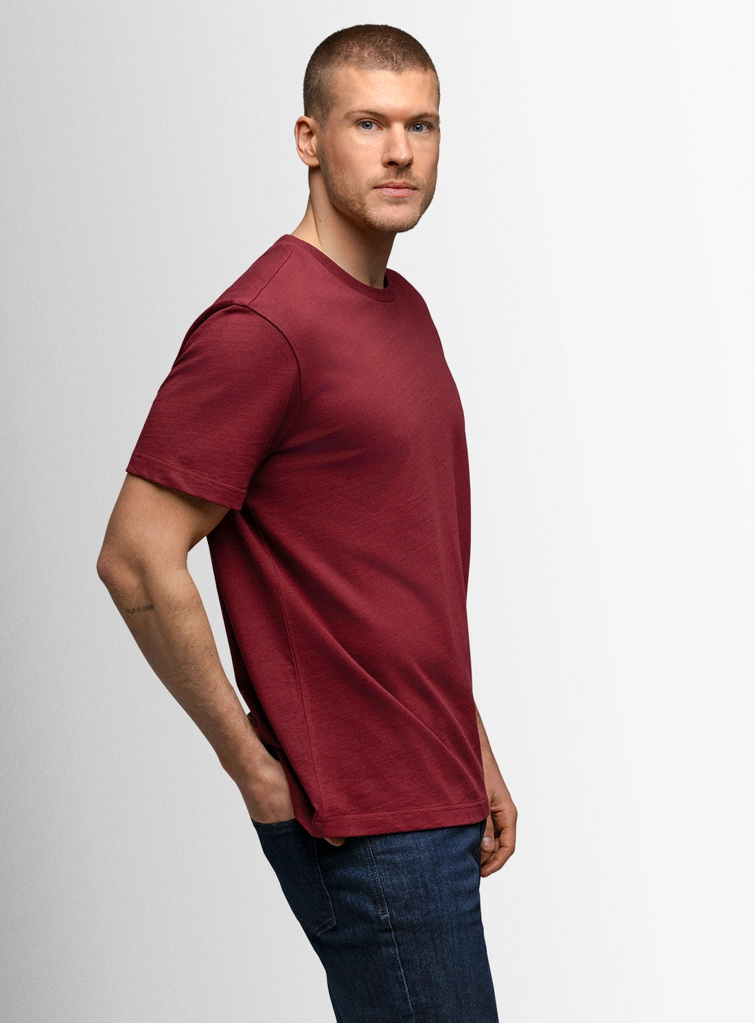 Man wearing a red t-shirt and blue jeans on a plain background