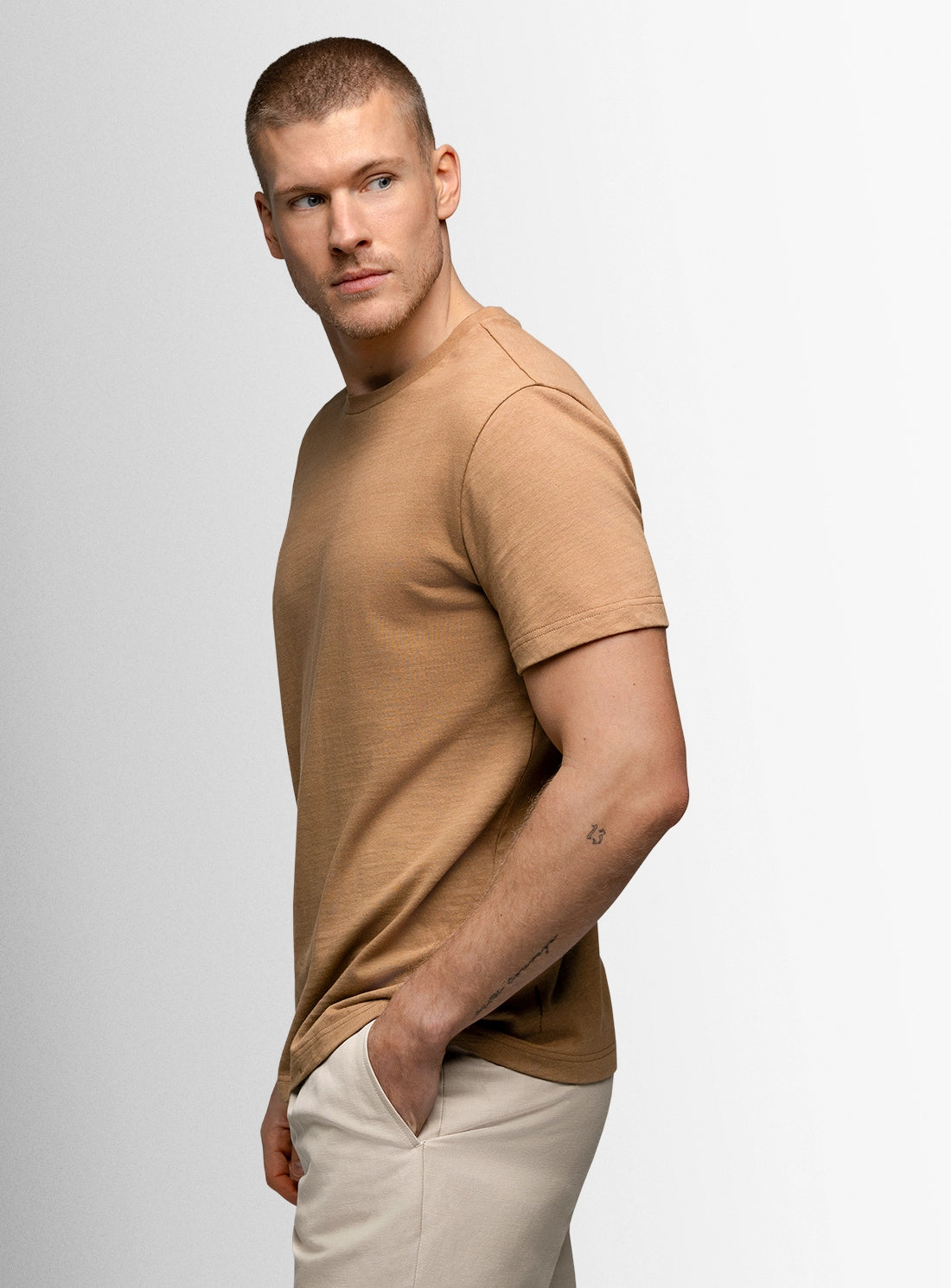 Man wearing a brown t-shirt and beige pants against a light gray background