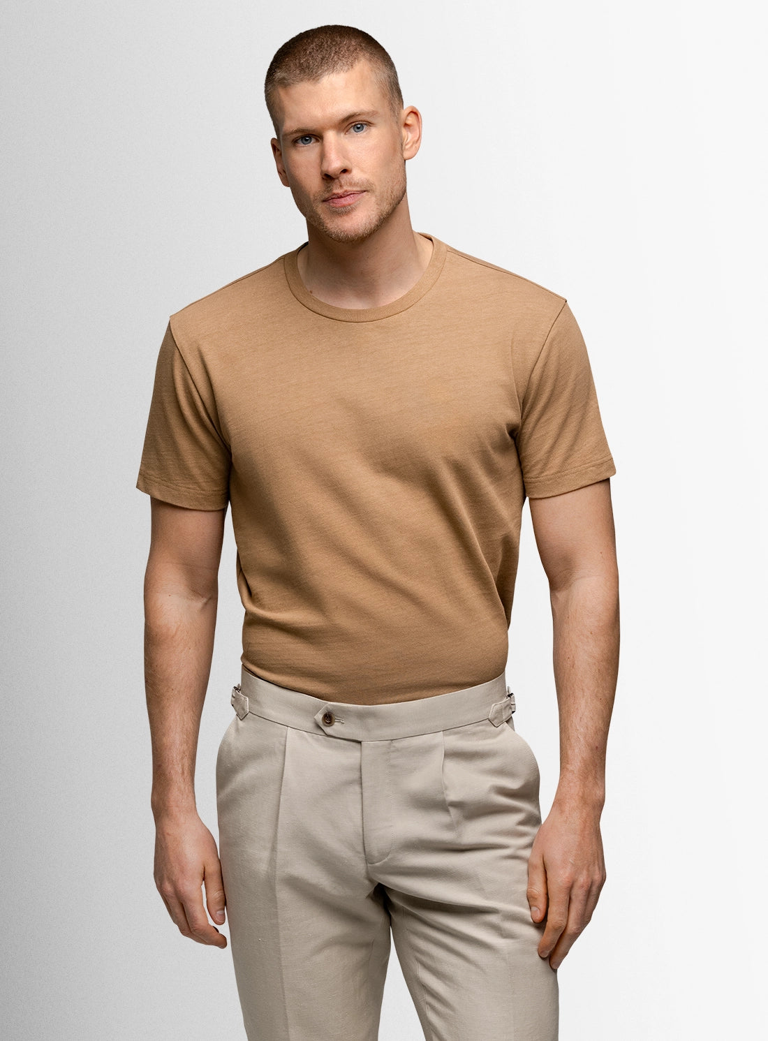 Man wearing a brown t-shirt and beige pants on a light gray background