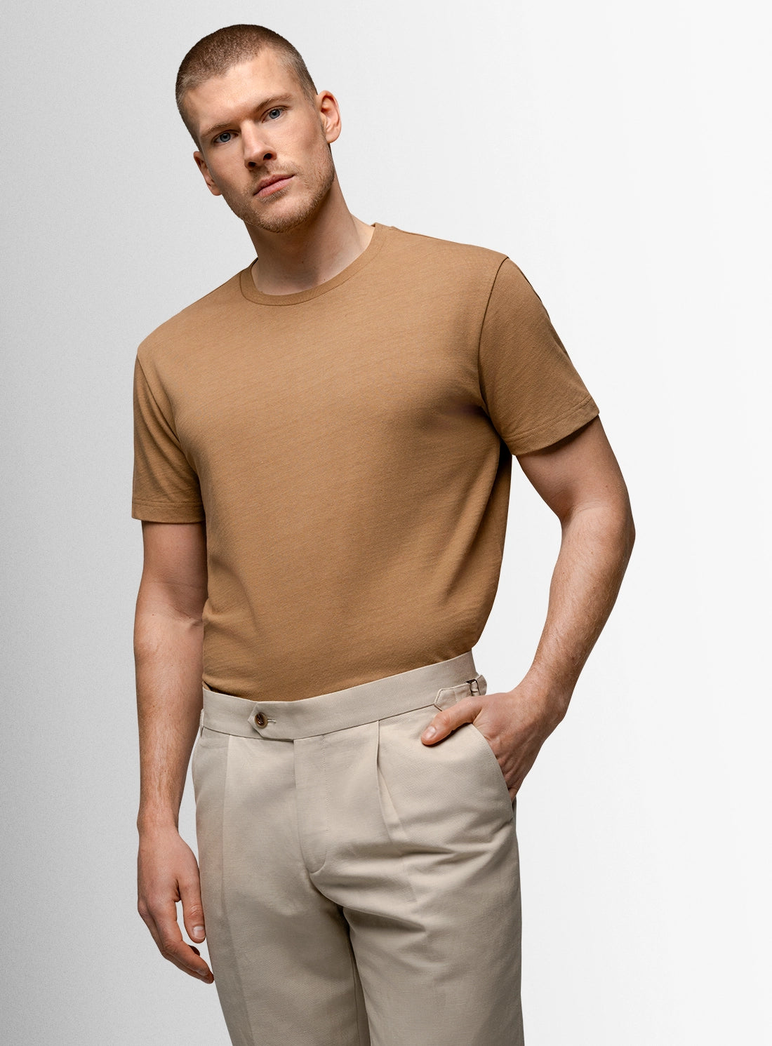 Man wearing a brown t-shirt and beige pants against a light gray background