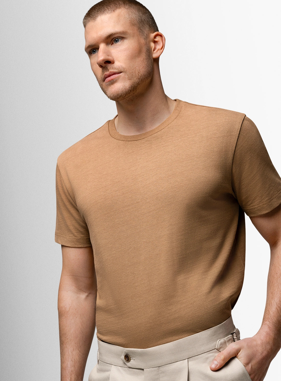 Man wearing a brown t-shirt and beige pants against a light gray background